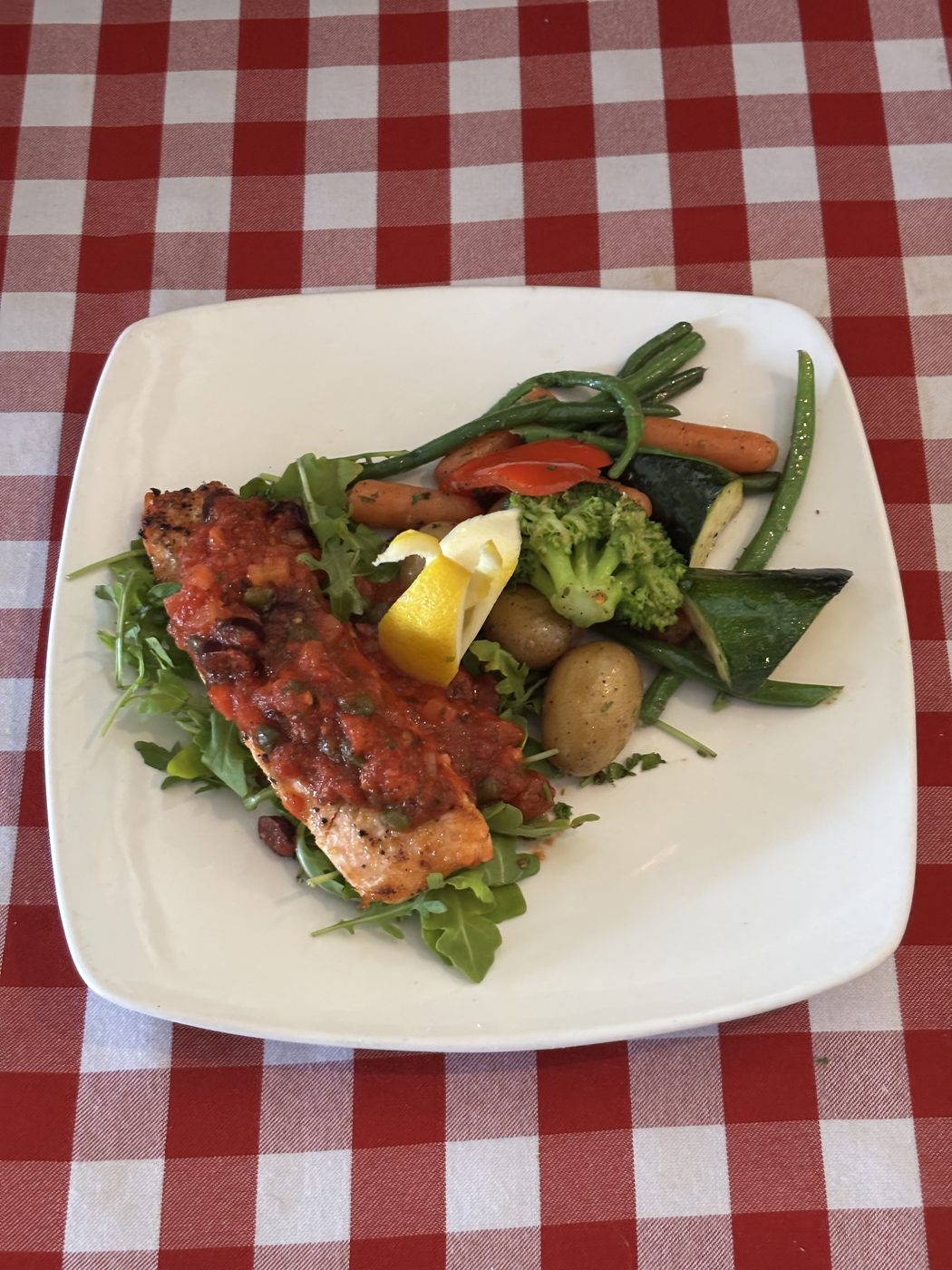 Grilled salmon fillet topped with tomato caper salsa on arugula